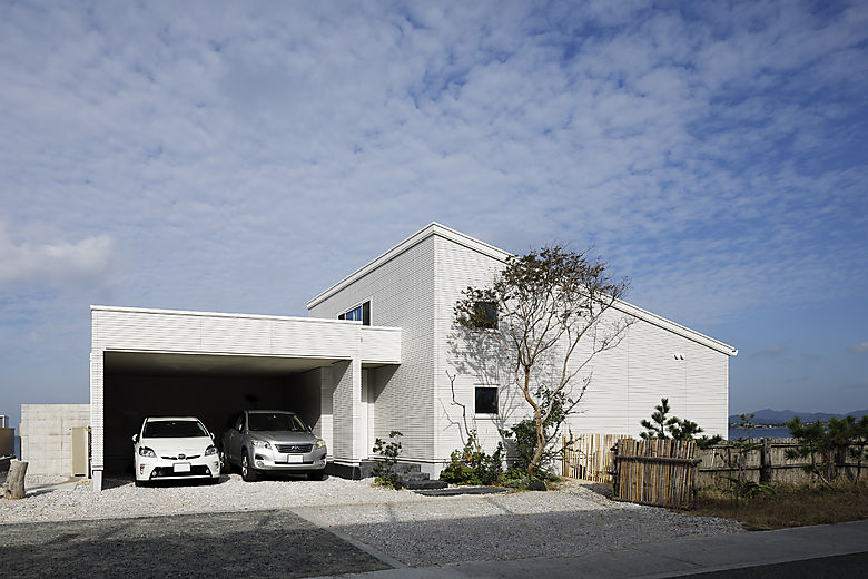 片流れ屋根の平屋のゆったりとした佇まい。潮風から守るようにガレージを配し、陶版外壁ベルバーンは青空に映える白を選択。